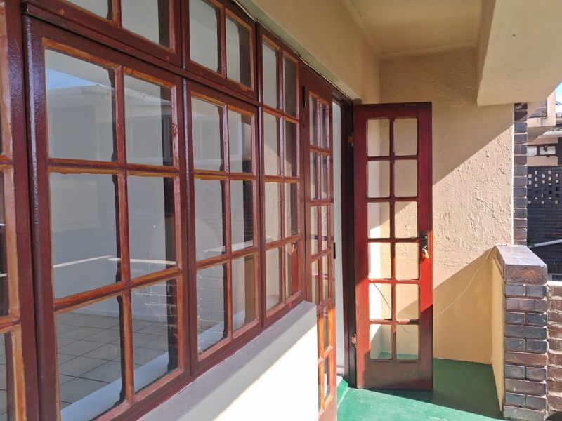 A covered balcony area featuring timber-framed glass doors and windows, with a brick balustrade and painted concrete flooring.