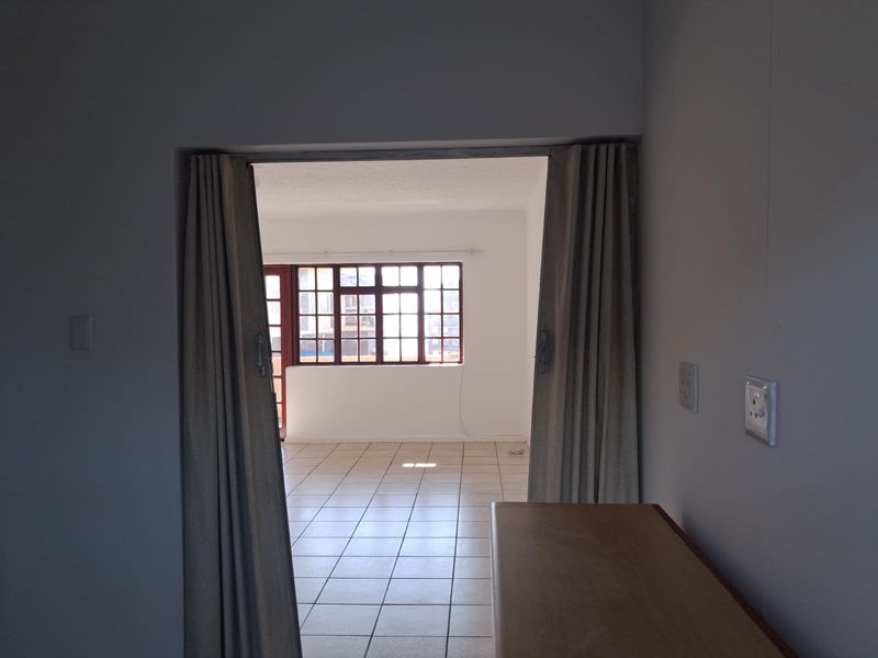 An empty living area featuring tiled flooring and a large multi-pane window, providing a bright and neutral space ready for personalization.
