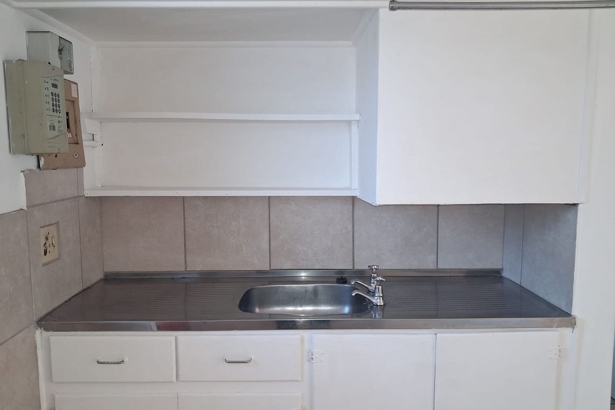 A compact kitchen area featuring a stainless steel sink, tiled backsplash, and basic built-in cabinetry with open shelving.