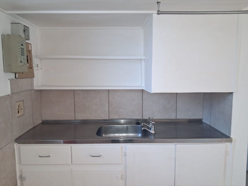 A compact kitchen area featuring a stainless steel sink, tiled backsplash, and basic built-in cabinetry with open shelving.