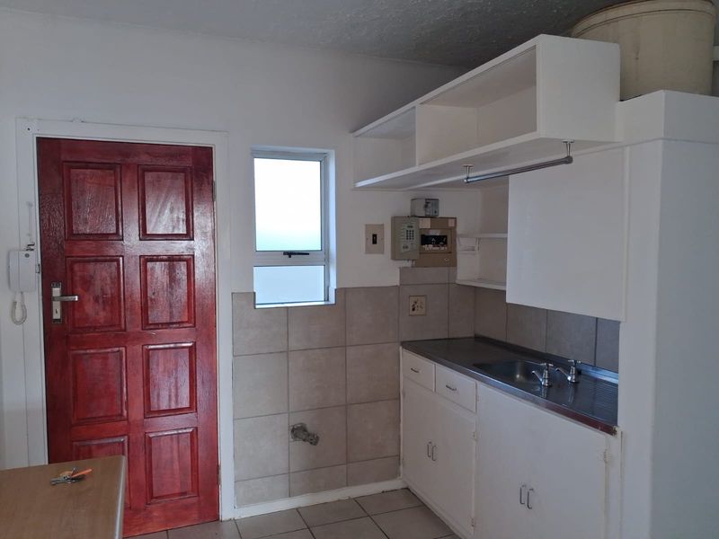 A functional scullery area featuring built-in cabinetry, a stainless steel sink, tiled splashback, and direct access to an exterior door.