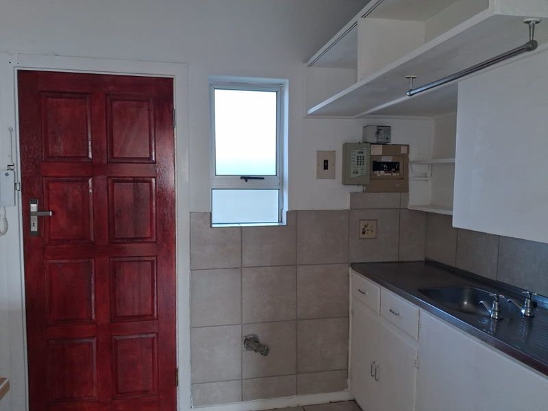 A functional laundry area featuring a stainless steel sink, tiled splashback, built-in cabinetry, and dedicated water connection point.