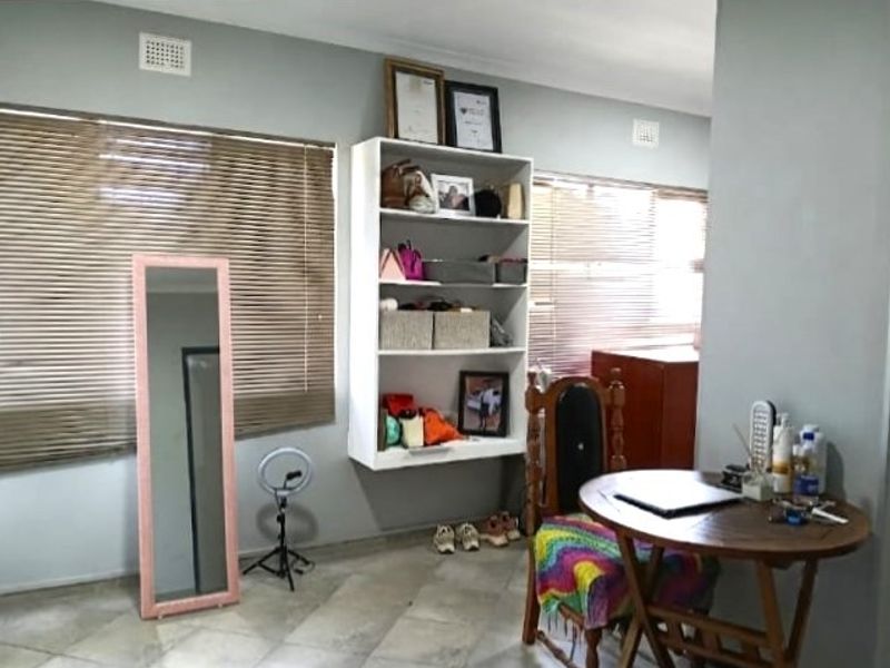 A bedroom featuring tiled flooring, wall-mounted shelving, and large windows with venetian blinds, offering a functional space with neutral wall finishes.