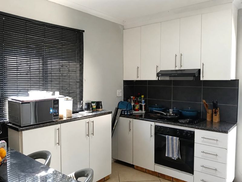 A functional kitchen featuring white cabinetry, dark countertops, a tiled backsplash, and integrated cooking appliances including an oven and extractor fan.