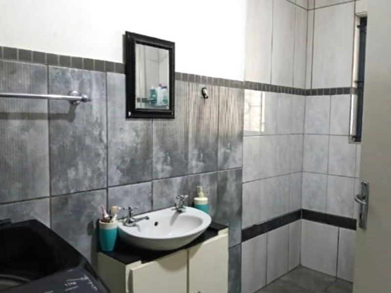 A functional bathroom featuring grey and white wall tiling, a vanity cabinet with a ceramic basin, and a window for natural light.