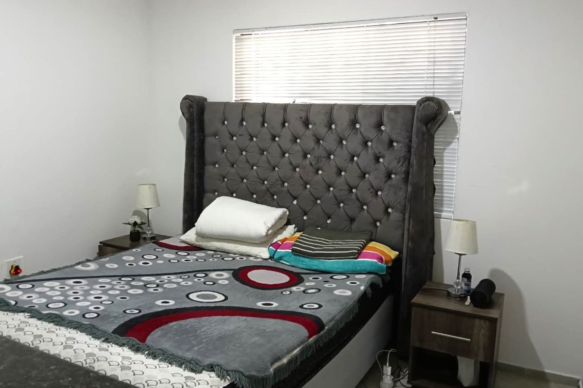 A well-maintained bedroom featuring neutral walls, tiled flooring, and a window fitted with venetian blinds.
