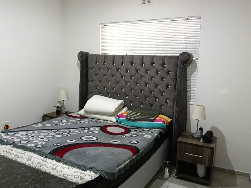 A well-maintained bedroom featuring neutral walls, tiled flooring, and a window fitted with venetian blinds.