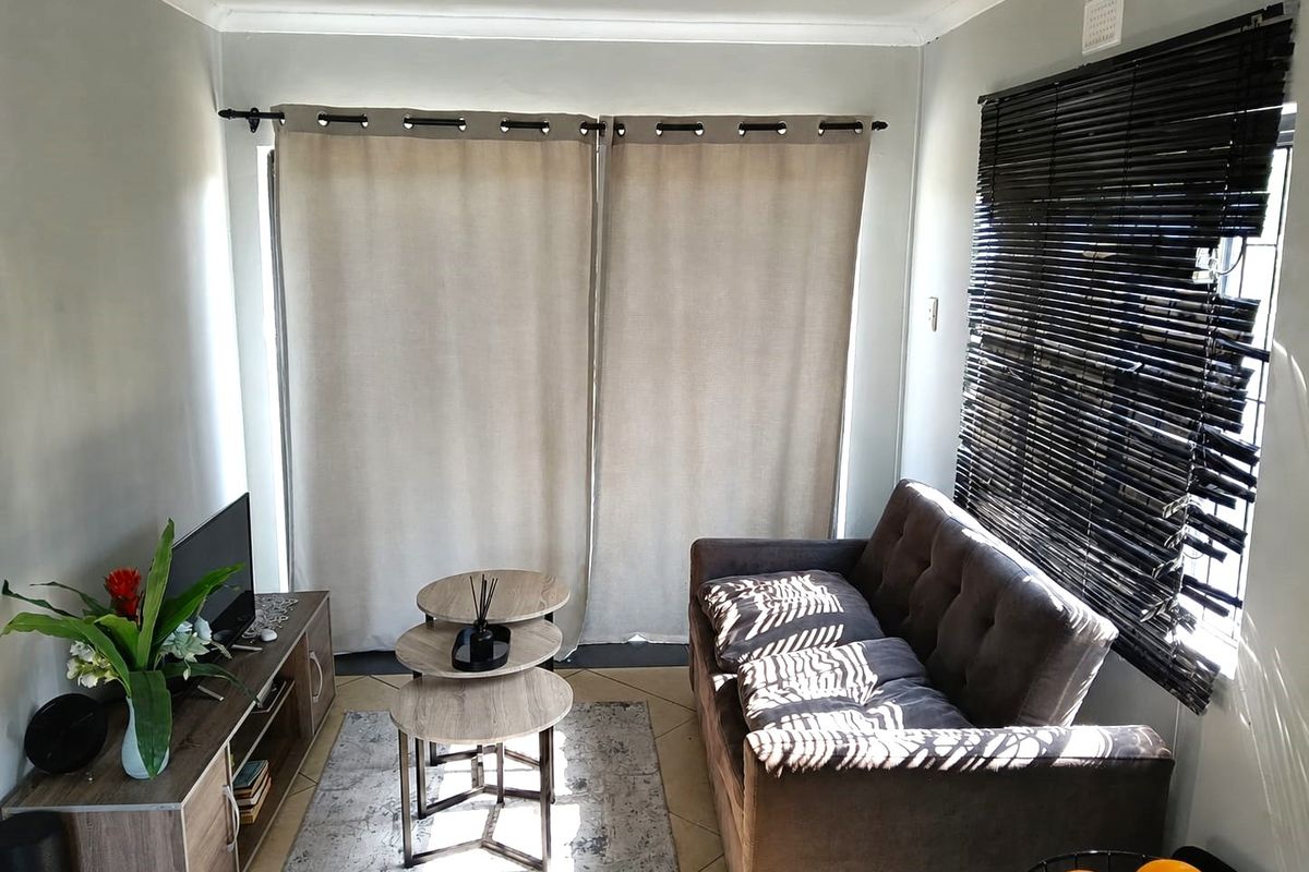 A compact living room featuring tiled flooring, coved ceilings, and window treatments including venetian blinds and curtain rods.