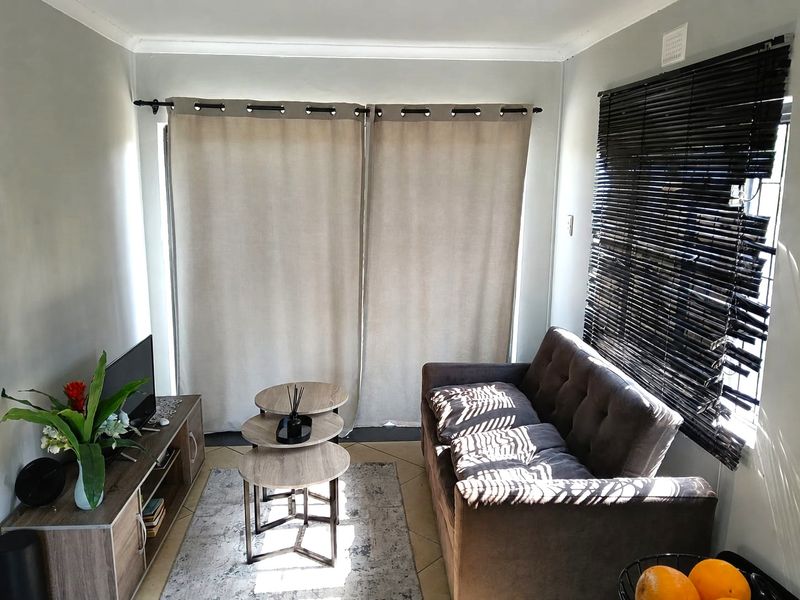 A compact living room featuring tiled flooring, coved ceilings, and window treatments including venetian blinds and curtain rods.