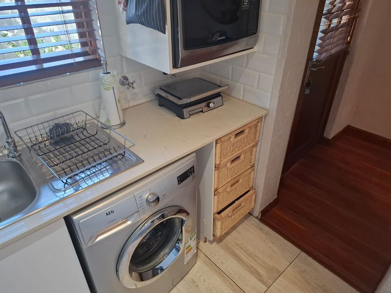 A functional laundry area featuring a stainless steel sink, subway tile backsplash, built-in microwave, and tiled flooring with timber blinds.