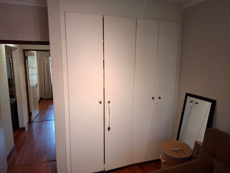 A bedroom featuring built-in white cupboards and laminate flooring, with a view through to an adjacent hallway.