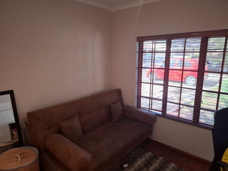 A compact living area featuring laminate flooring and large windows with wooden venetian blinds, offering natural light and a view of the exterior.