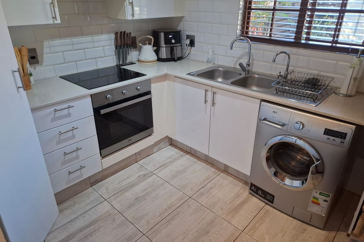 A well-maintained kitchen featuring white cabinetry, subway tile backsplash, stone countertops, an electric hob, built-in oven, and integrated laundry appliance space.