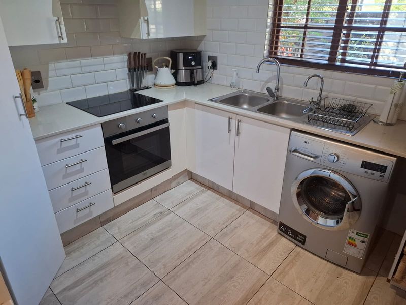 A well-maintained kitchen featuring white cabinetry, subway tile backsplash, stone countertops, an electric hob, built-in oven, and integrated laundry appliance space.