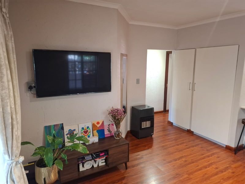 A living room area featuring laminate flooring, built-in storage cupboards, and a wall-mounted television point.
