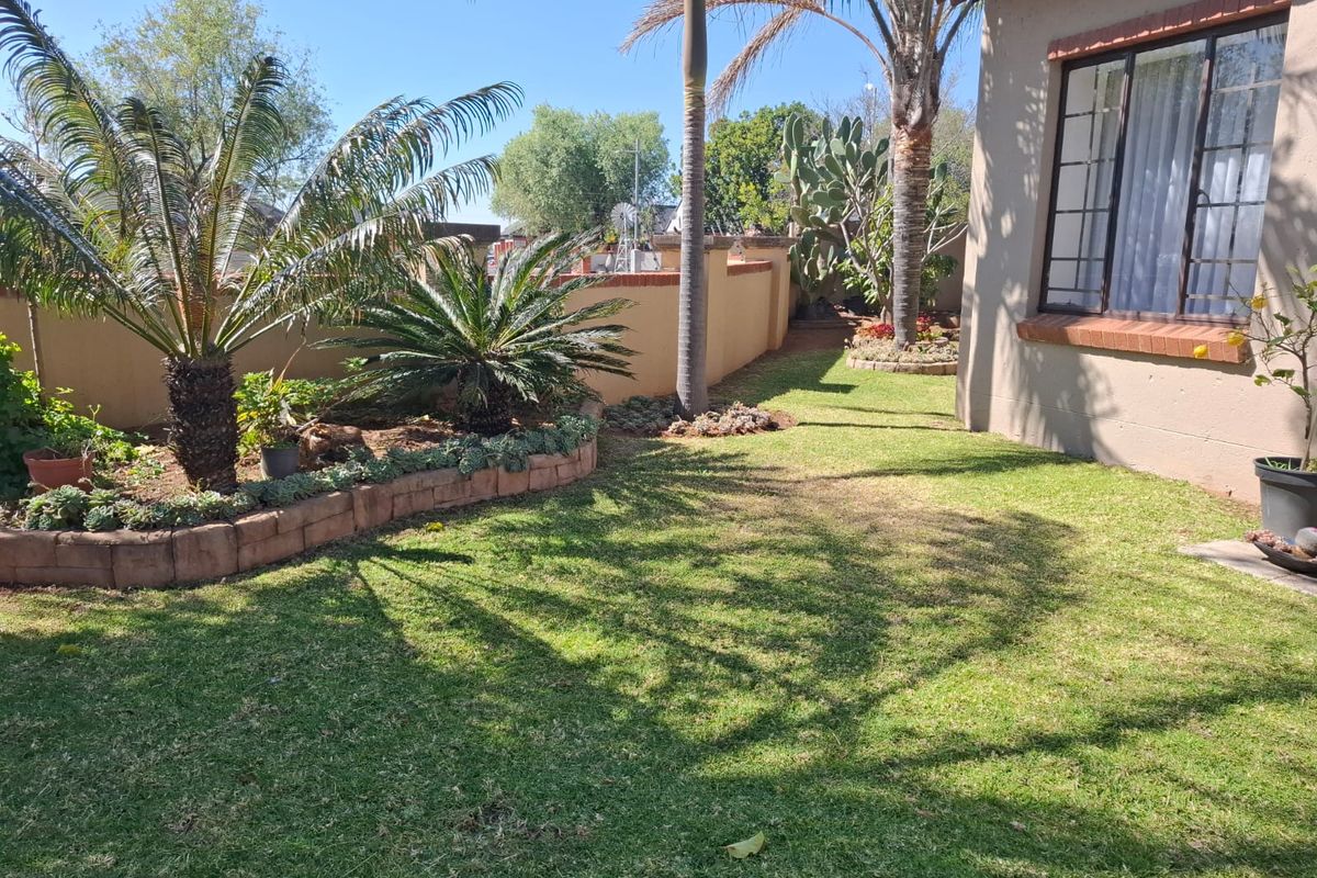 A well-maintained rear garden area featuring established landscaping, brick-edged garden beds, and a clear view of the townhouse exterior wall and window.