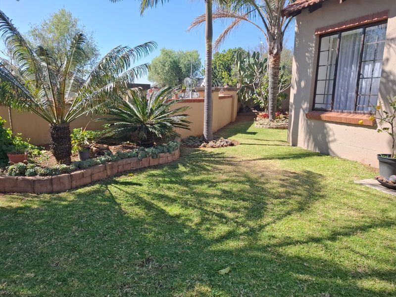 A well-maintained rear garden area featuring established landscaping, brick-edged garden beds, and a clear view of the townhouse exterior wall and window.