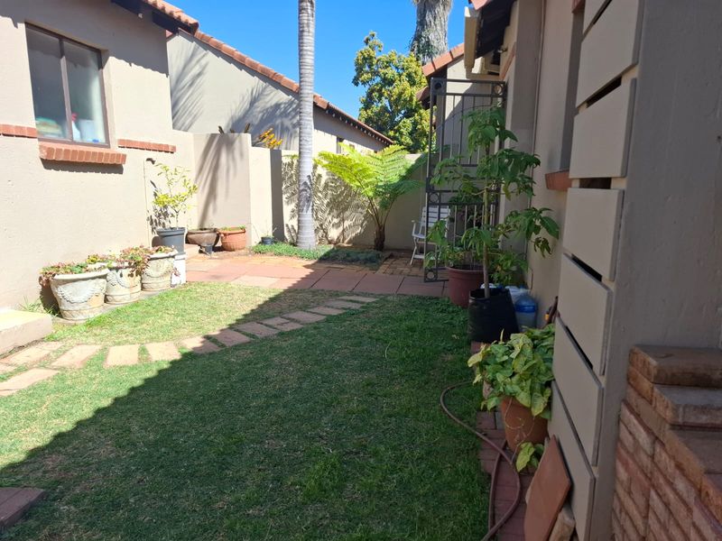 A private rear garden area featuring a small lawn, paved pathway, and boundary walls, providing a quiet outdoor space for the townhouse.
