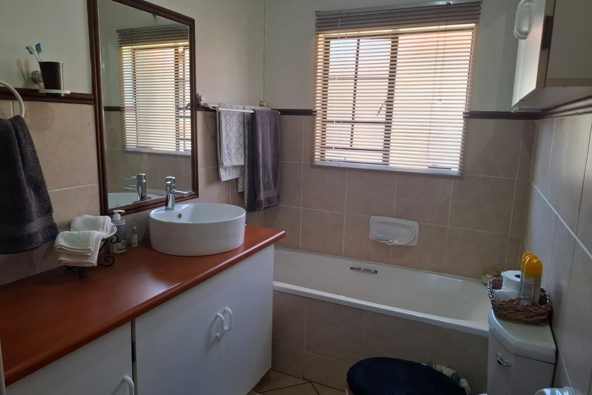 A functional bathroom featuring a vanity with a vessel sink, a bathtub, and neutral wall tiling.