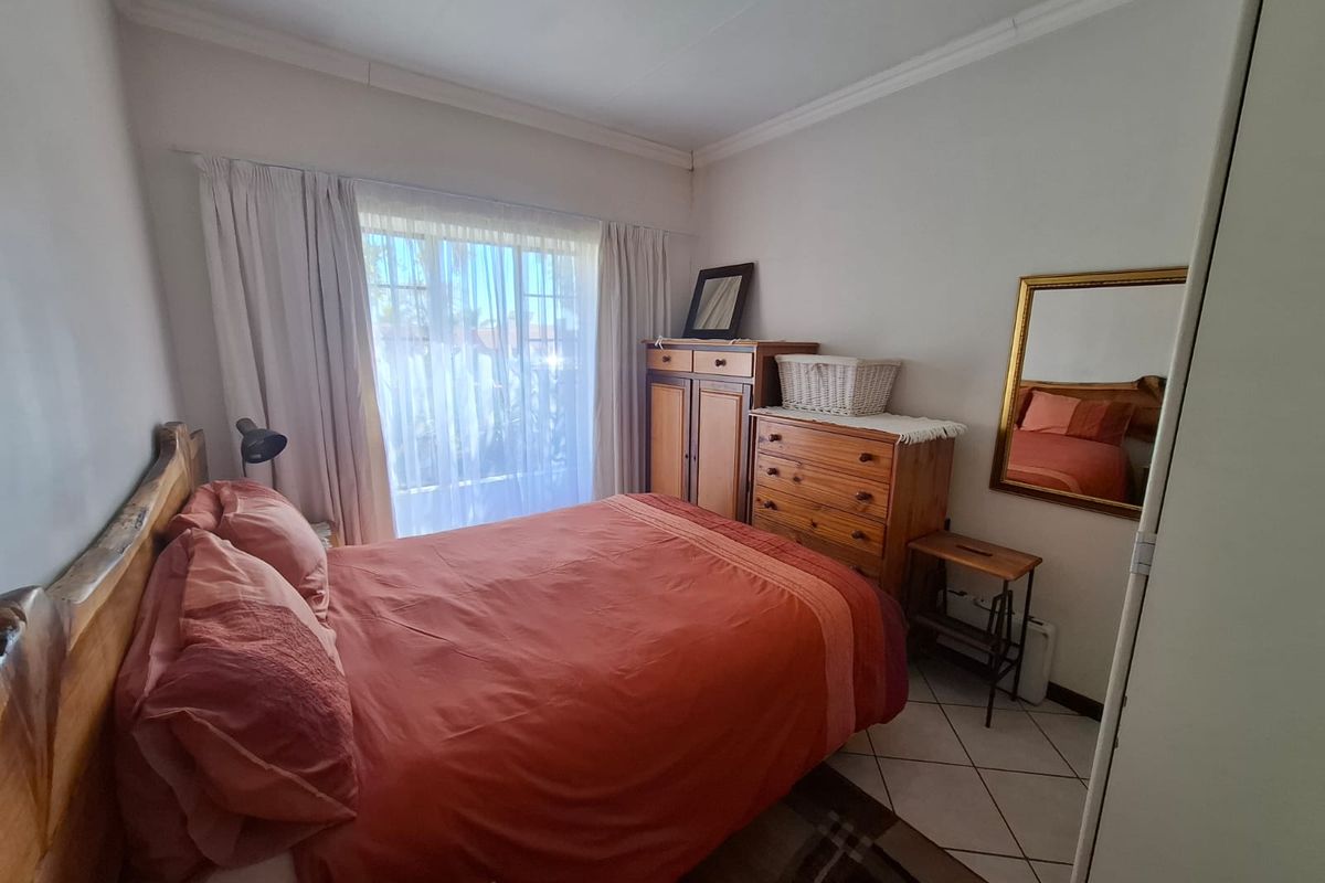 A functional bedroom featuring tiled flooring, a built-in wardrobe, and natural light through a large window with curtains.