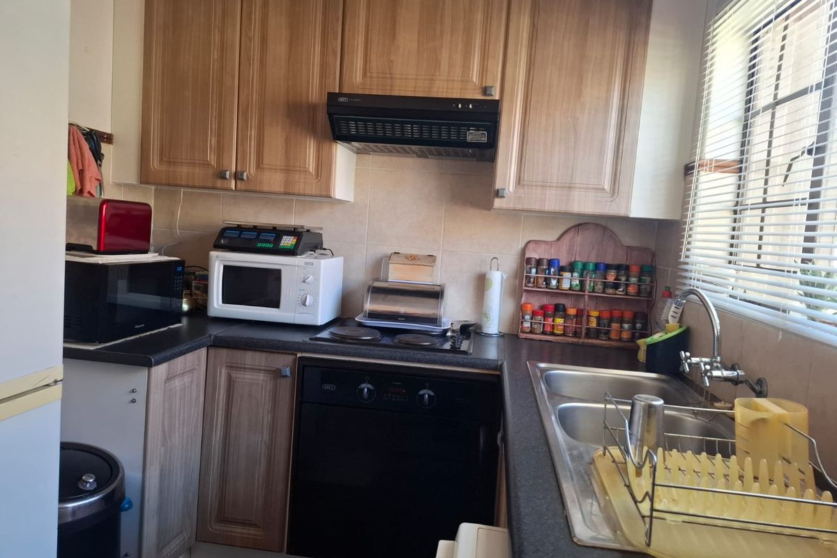 A functional kitchen featuring wood-look laminate cabinetry, a built-in oven with hob, extractor fan, and a double bowl stainless steel sink with tiled backsplash.