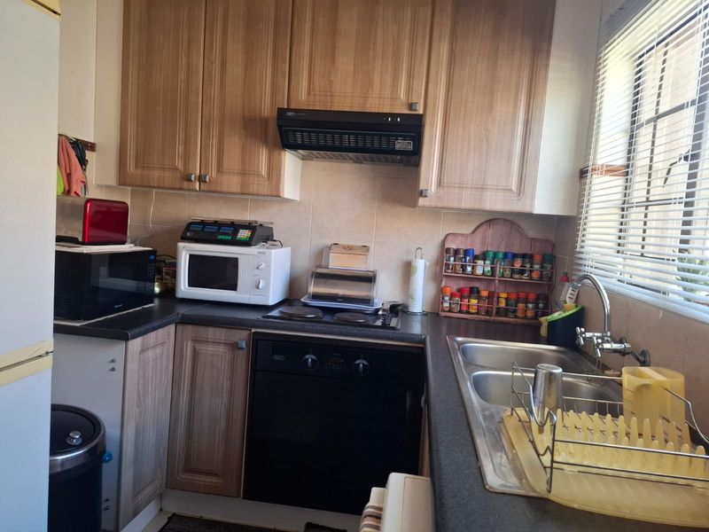 A functional kitchen featuring wood-look laminate cabinetry, a built-in oven with hob, extractor fan, and a double bowl stainless steel sink with tiled backsplash.