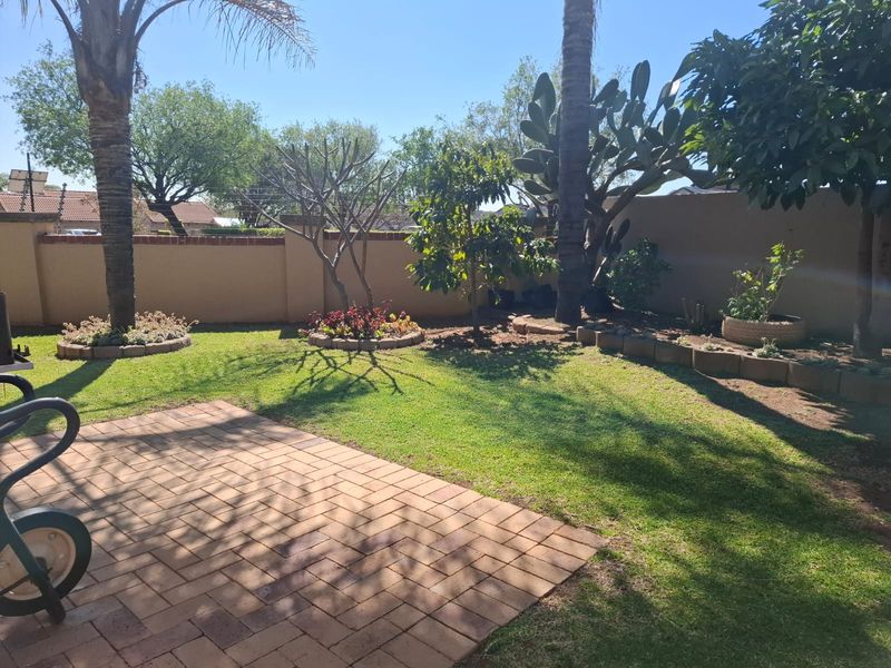 A private rear garden featuring a brick-paved patio area, established trees, and perimeter boundary walls.