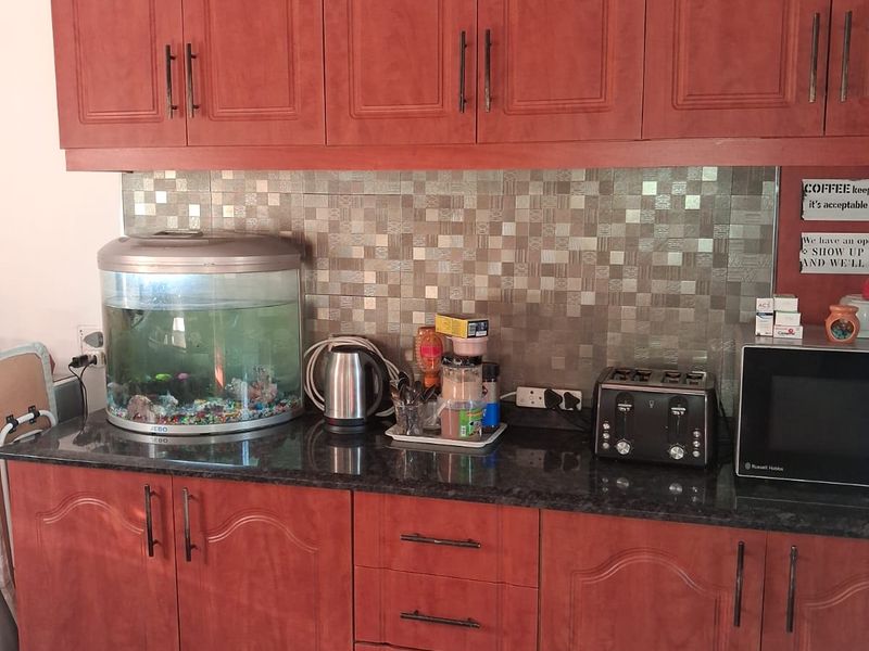A functional kitchen featuring warm-toned laminate cabinetry, dark granite countertops, and a decorative mosaic tile backsplash.