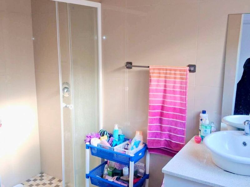 A functional bathroom featuring a glass shower enclosure, a modern vessel sink with vanity storage, and neutral wall tiling.