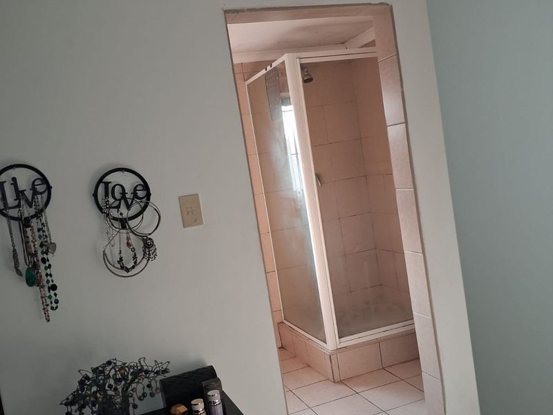 A functional bathroom featuring a tiled shower enclosure with a glass door, accessible from the adjacent room.