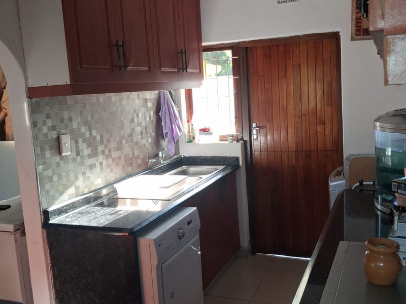 A functional kitchen featuring built-in cabinetry, dark laminate countertops, a tiled backsplash, and tiled flooring with direct access to an exterior timber door.