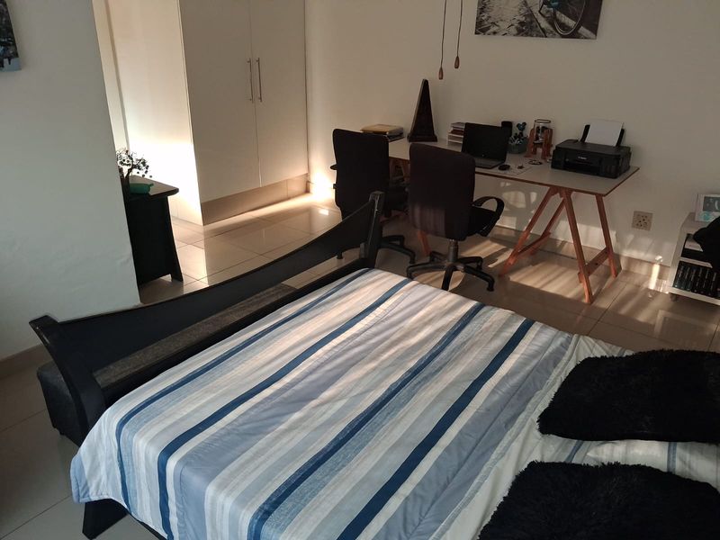 A bedroom featuring tiled flooring and a built-in wardrobe, currently utilized as a combined sleeping and workspace area.