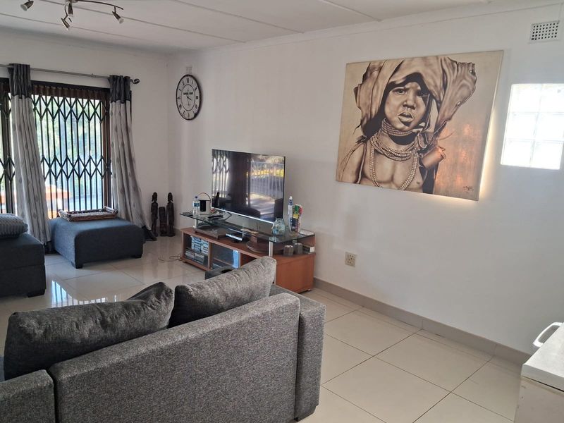A well-lit living room featuring neutral tiled flooring, a security gate over the sliding door, and a glass block window for natural light.