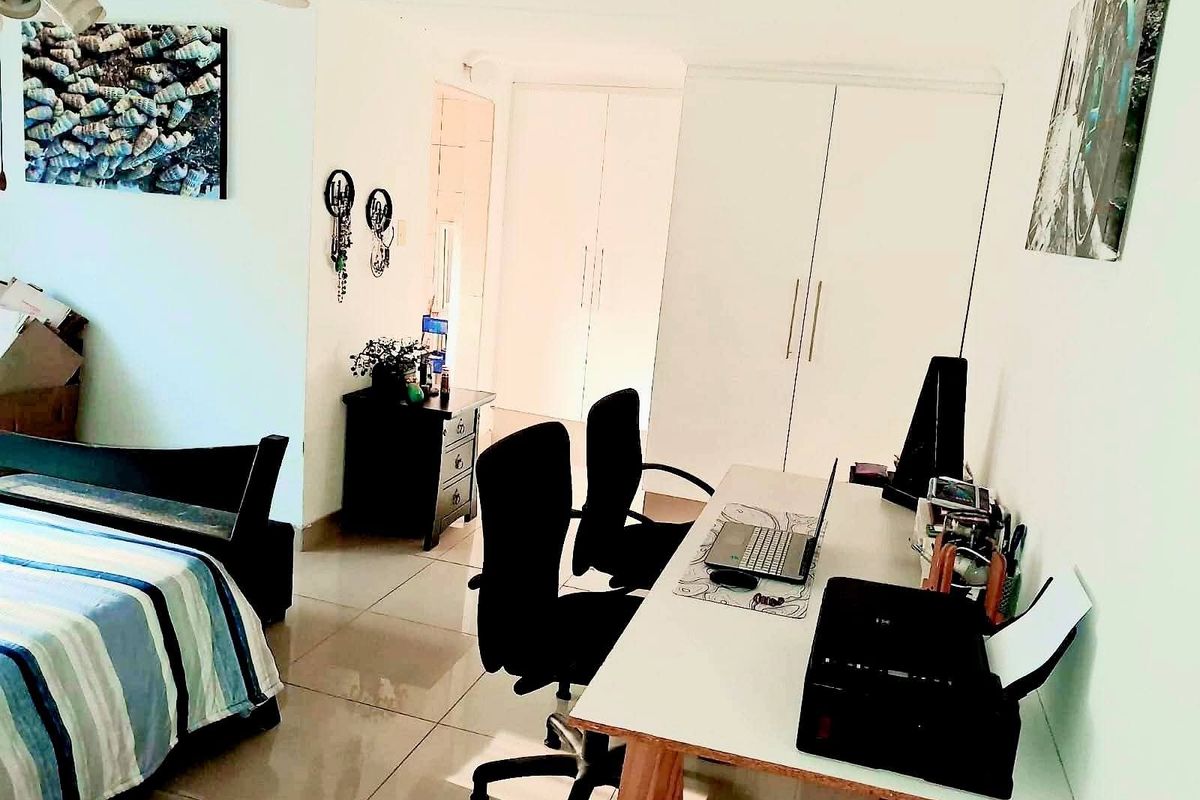 A bedroom featuring built-in cupboards, tiled flooring, and a ceiling fan, currently utilized as a combined sleeping and workspace area.