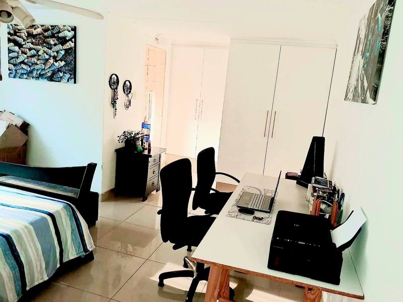 A bedroom featuring built-in cupboards, tiled flooring, and a ceiling fan, currently utilized as a combined sleeping and workspace area.