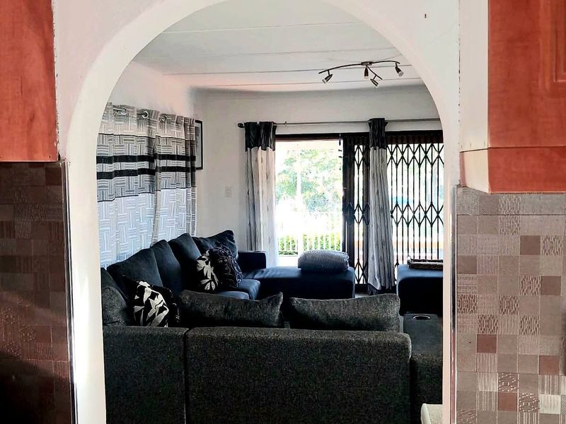 Open plan living area viewed through an arched doorway, featuring tiled floors, track lighting, and access to an outdoor space via sliding glass doors.