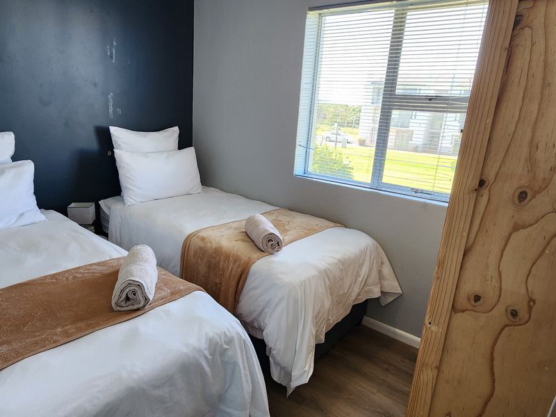 A compact bedroom featuring laminate flooring, a window with venetian blinds, and a natural wood door.
