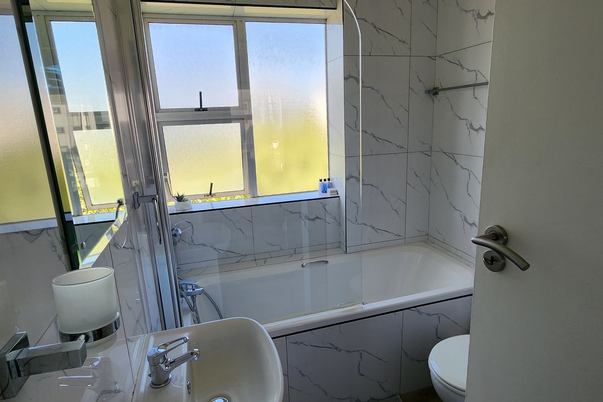 Modern bathroom featuring marble-look wall tiles, a bathtub with a glass shower screen, a basin with a mixer tap, and a toilet.