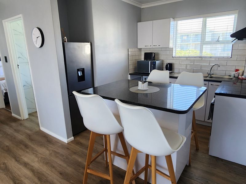 A modern kitchen featuring granite countertops, subway tile backsplash, and white cabinetry, seamlessly integrated with a breakfast bar area.