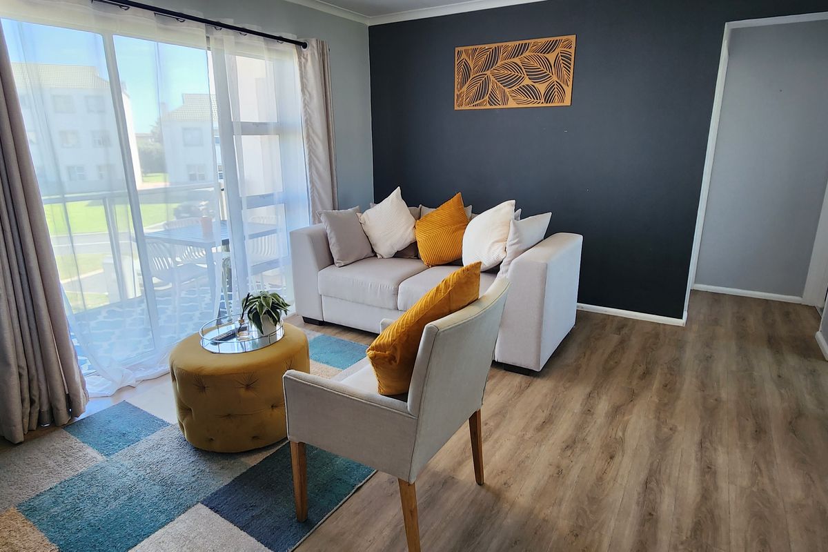 A bright living room featuring laminate flooring, a dark accent wall, and a large sliding glass door providing access to an outdoor balcony area.