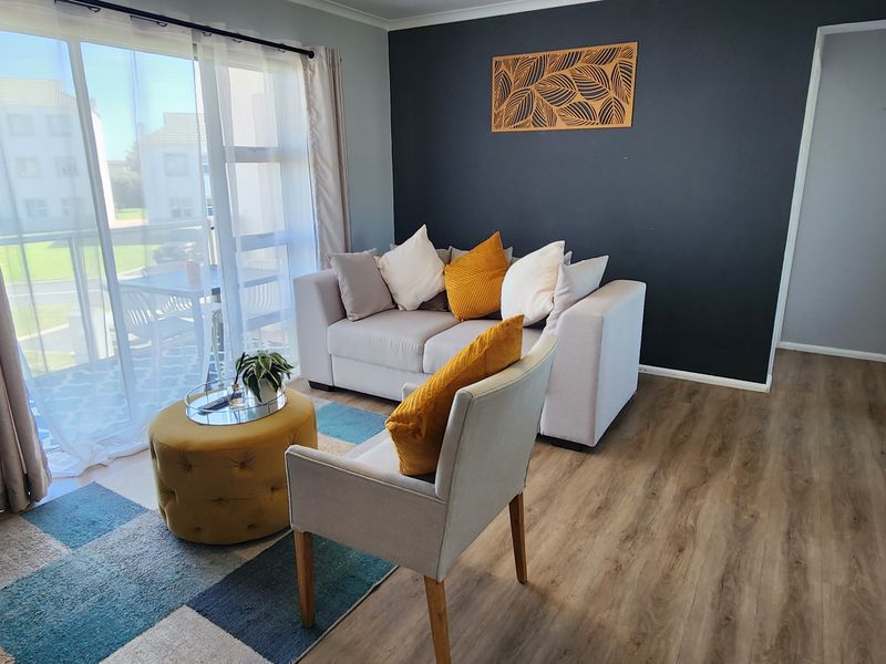A bright living room featuring laminate flooring, a dark accent wall, and a large sliding glass door providing access to an outdoor balcony area.
