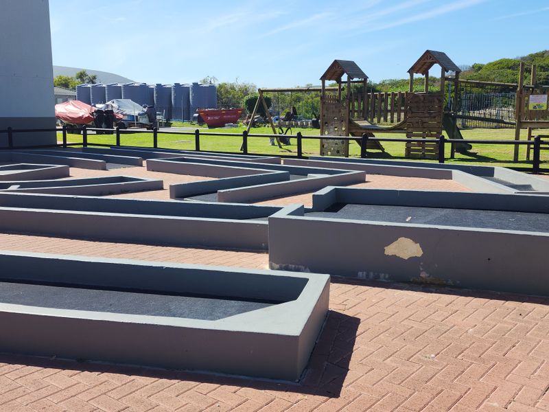 Outdoor miniature golf course area featuring paved pathways, timber fencing, and an adjacent children's playground.