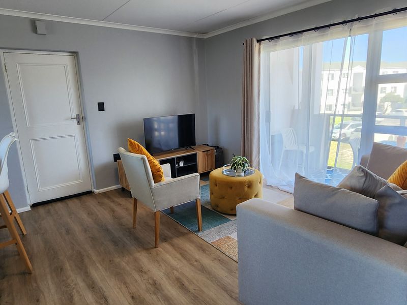 Open plan living area featuring laminate flooring, a breakfast bar, and large sliding glass doors providing access to the balcony.