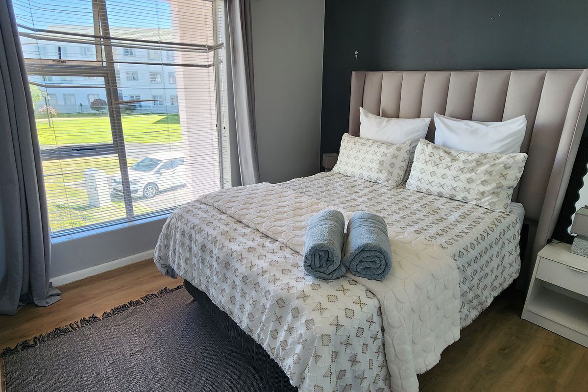 A well-lit bedroom featuring laminate flooring and a large window with venetian blinds, providing natural light and a view of the exterior.