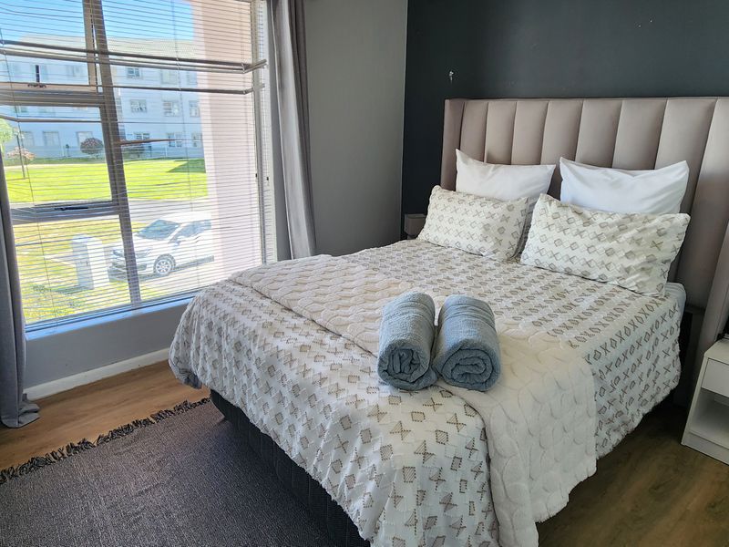 A well-lit bedroom featuring laminate flooring and a large window with venetian blinds, providing natural light and a view of the exterior.