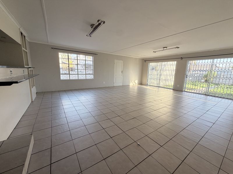 Spacious open-plan living area featuring tiled flooring, security gates, and sliding doors leading to the exterior, offering a blank canvas for renovation.