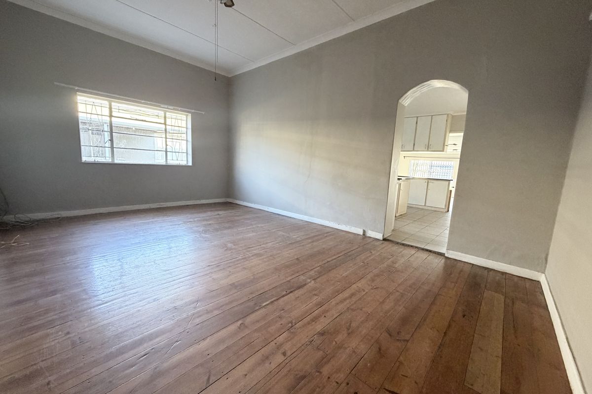 Spacious living room featuring original hardwood flooring, a ceiling fan, and an arched entryway leading into the kitchen area.