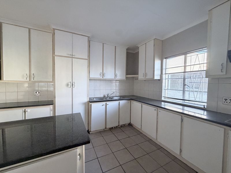 A functional kitchen featuring white built-in cabinetry, dark granite countertops, tiled flooring, and a double basin sink with a window view.