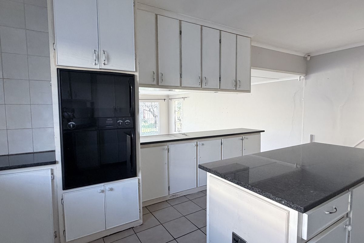 A dated kitchen featuring white cabinetry, granite countertops, a central island, and built-in oven, requiring cosmetic updates to modernize the space.
