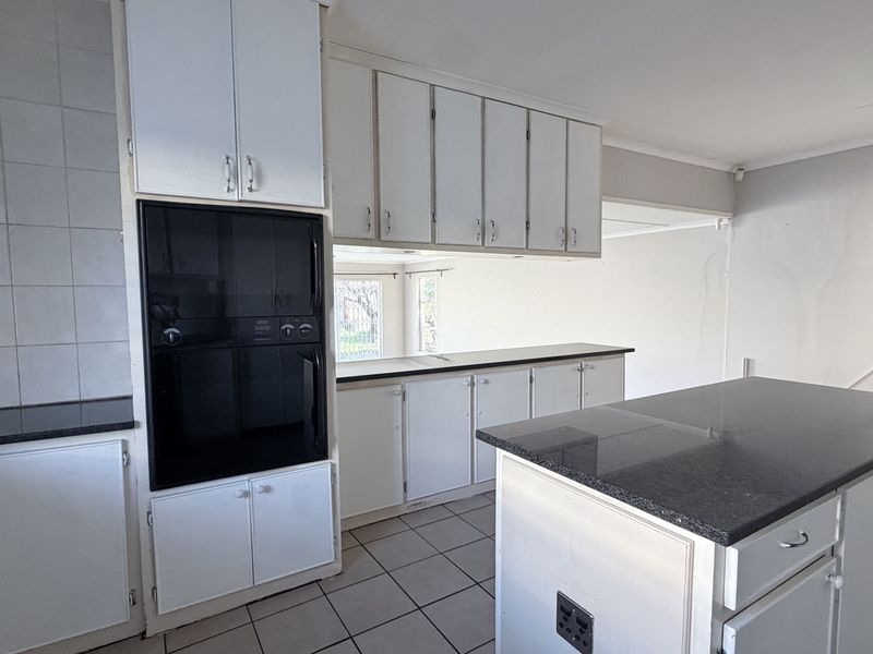 A dated kitchen featuring white cabinetry, granite countertops, a central island, and built-in oven, requiring cosmetic updates to modernize the space.